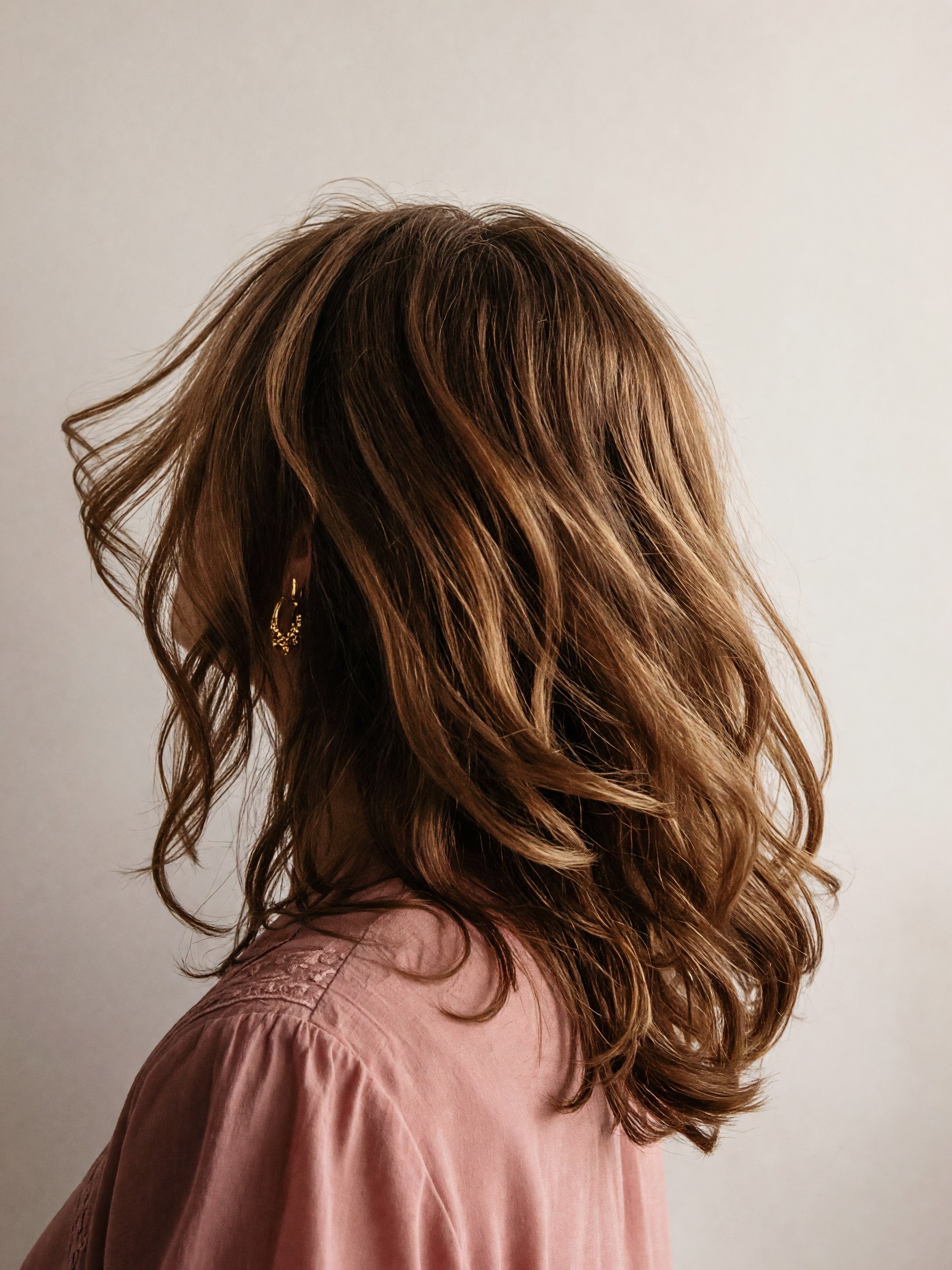 A soft blowout of dark honey waves, seen from behind the shoulder.